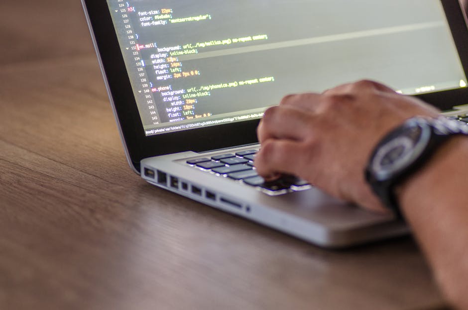 Photograph of a computer monitor displaying a coding script with colorful syntax highlighting, including lines of JavaScript or similar programming language. In the background, a partially visible mov
